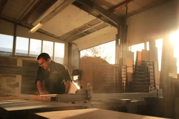 Ein Schreiner arbeitet an einer Kreissäge in einer sonnendurchfluteten Werkstatt.