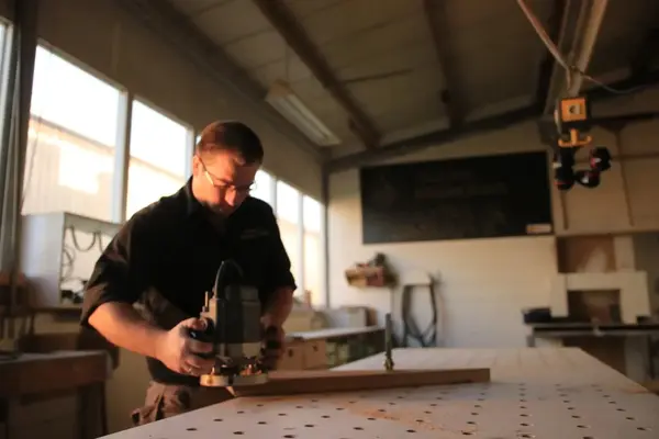 Ein Schreiner arbeitet konzentriert mit einer Oberfräse in einer hellen Werkstatt.