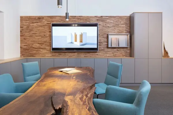 Moderner Konferenzraum mit Massivholztisch, blauen Stühlen und Steinwand als Akzent.
